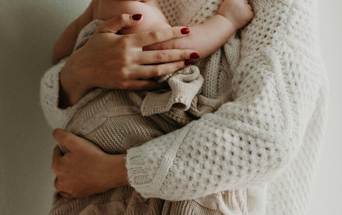 Mother receiving Mummy MOT consultation while holding her baby, emphasising postnatal care and support.